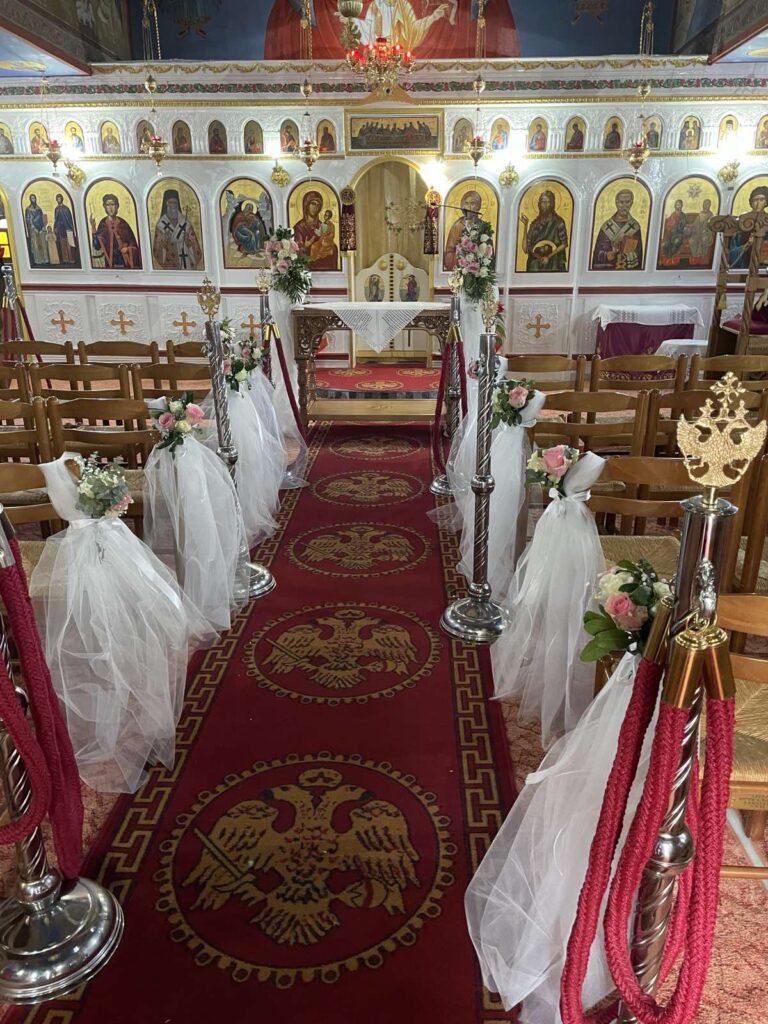 Διάδρομος εκκλησίας με κόκκινο χαλί, γάζες και λουλούδια για γάμο